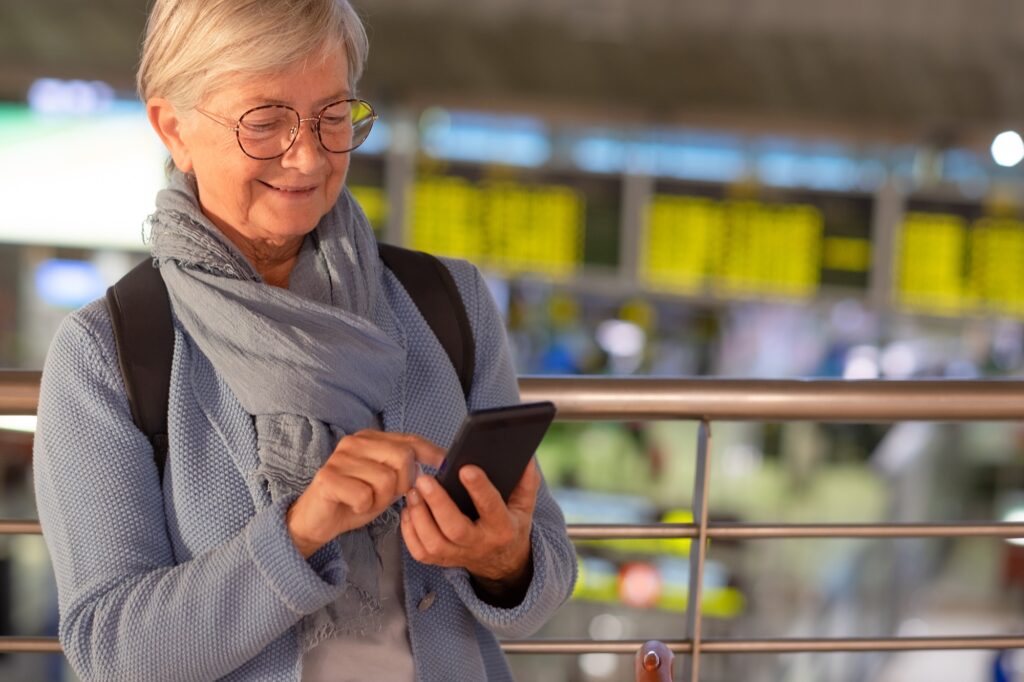 Smiling senior woman in aeroport waiting for boarding using mobile phone connection to send message