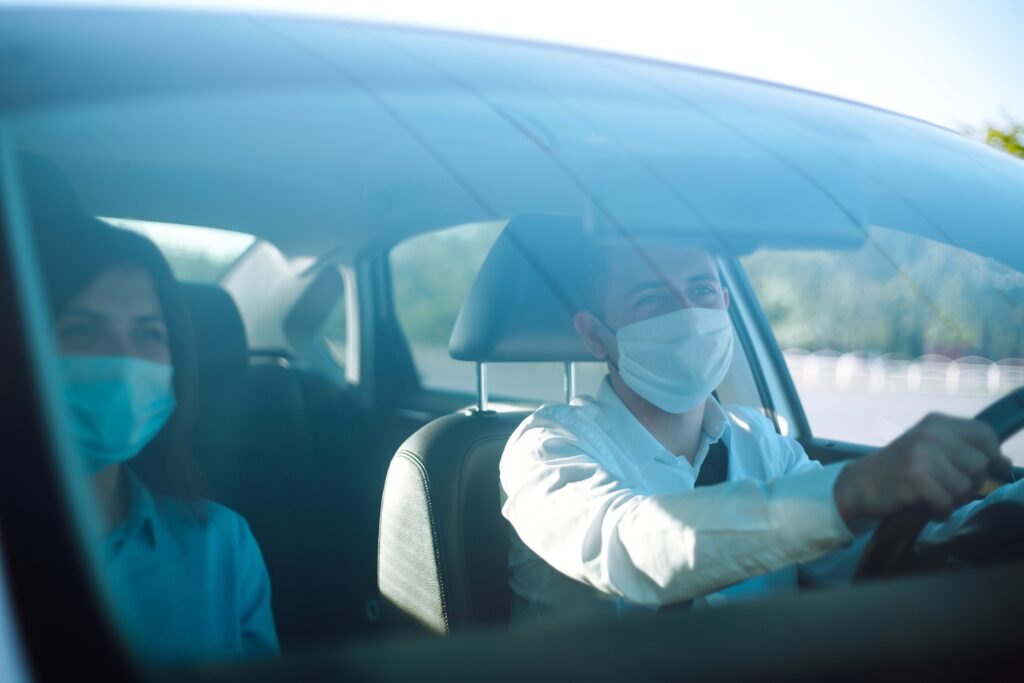 Young man and woman driving in a car during coronavirus quarantine in medical masks. Safe taxi